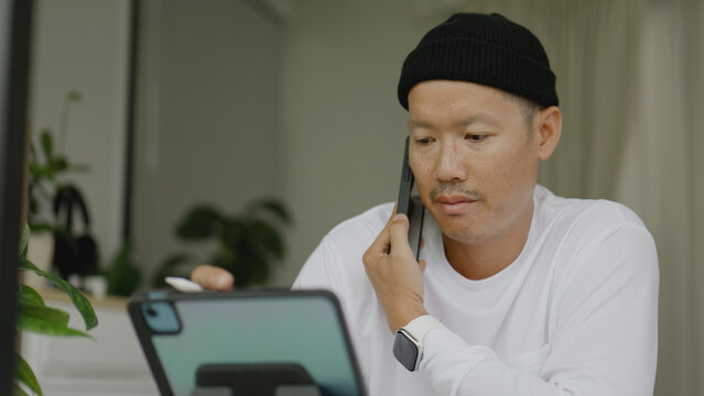 Asian man using smart phone and tablet on the table in home.  - Powered by Adobe