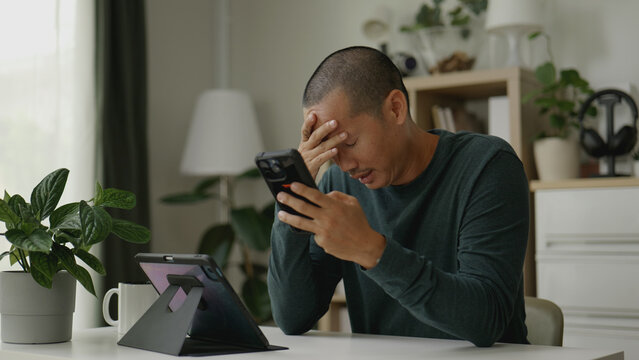 Asian man looking upset after reading a message on his smartphone.