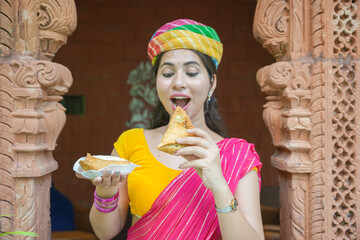 Young happy indian woman wearing sari and turban eating crispy spicy samosa street food of india.