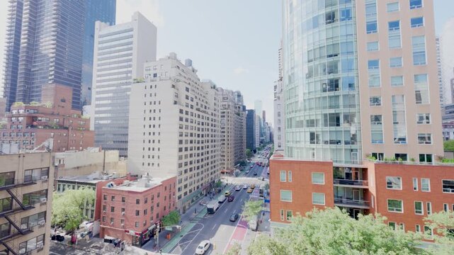 Tall residential facades rise beside a city street, with pale walls and rows of windows framed against the blue daylight sky. The urban forms show contrasting architectural details in the urban scene.