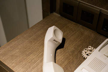 Close-up view of a classic white telephone handset placed on a wooden desk in a modern room,...