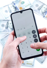 Manos haciendo cálculo en aplicación de calculadora de teléfono móvil con dólares de fondo. 