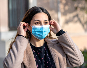 Young woman adjusting her blue protective face mask outdoors, reflecting public health, safety, and personal responsibility during challenging times.