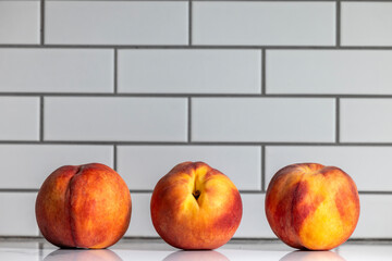 Three Colorful Ripe Peaches lined up on a kitchen counter backdrop