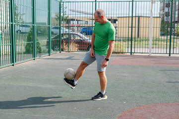 Obraz premium A young man, a football and basketball coach, wearing a bright green T-shirt, is playing ball on a sports court, waiting for his student partner. Sports, activity. Training with a ball on a sports fie