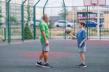 Father teaches his son how to play basketball. The boy throws the ball into the hoop at the playground. Generation. Sports. Hobbies