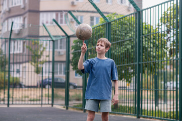 A teenage boy in a blue T-shirt is twirling basketball on his finger. The concept of sport and a...