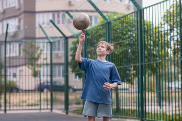 A teenage boy in a blue T-shirt is twirling basketball on his finger. The concept of sport and a...