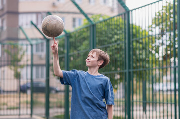 A teenage boy in a blue T-shirt is twirling basketball on his finger. The concept of sport and a...