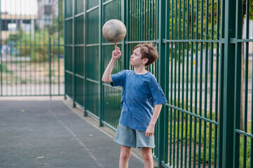 A teenage boy in a blue T-shirt is twirling basketball on his finger. The concept of sport and a...