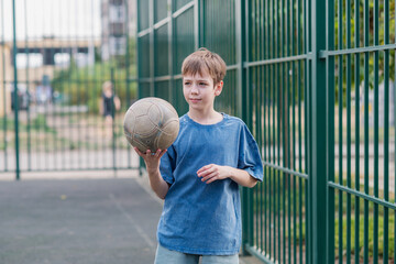 A teenage boy in a blue T-shirt is twirling basketball on his finger. The concept of sport and a...