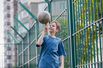 A teenage boy in a blue T-shirt is twirling basketball on his finger. The concept of sport and a...