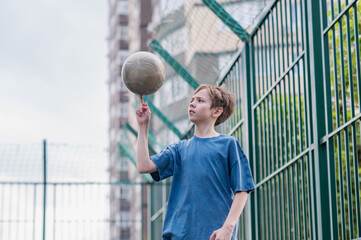 A teenage boy in a blue T-shirt is twirling basketball on his finger. The concept of sport and a...