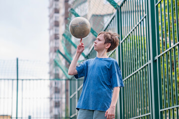 A teenage boy in a blue T-shirt is twirling basketball on his finger. The concept of sport and a...