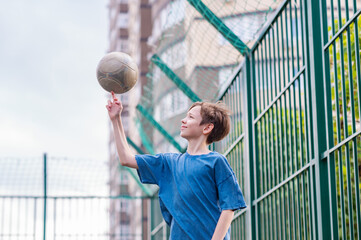 A teenage boy in a blue T-shirt is twirling basketball on his finger. The concept of sport and a...