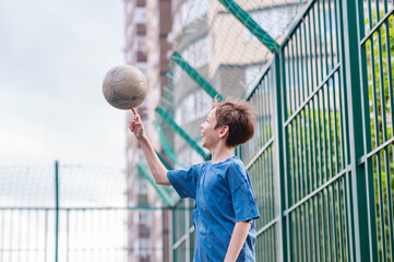A teenage boy in a blue T-shirt is twirling basketball on his finger. The concept of sport and a...