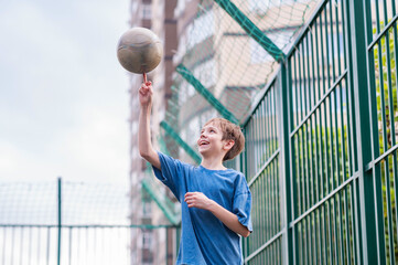 A teenage boy in a blue T-shirt is twirling basketball on his finger. The concept of sport and a...