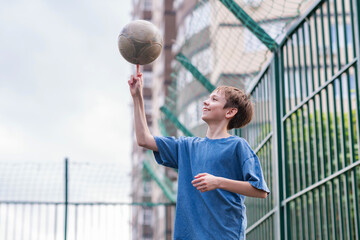 A teenage boy in a blue T-shirt is twirling basketball on his finger. The concept of sport and a...