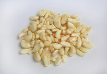 Peeled garlic cloves on white plate against wooden background, preparation process of garlic for cooking.
