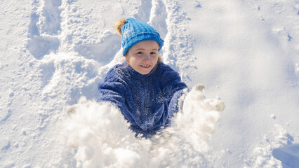 Kid and snow in the park. Kid plays joyfully in snowfall. Winter kids portrait. Snowflakes on happy...