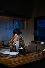 Exhausted worker staying up late at home, sitting at table with laptop and documents