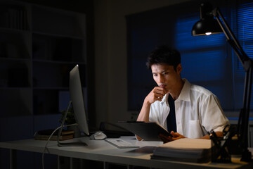 Focused businessman working late at night in office, reviewing documents under desk lamp