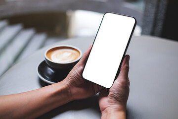 Mockup image of a woman holding and using mobile phone with blank desktop screen in cafe