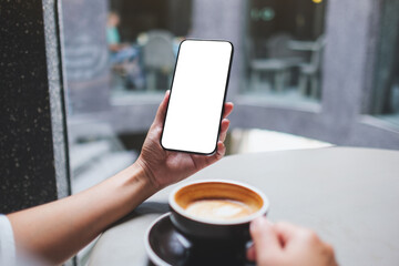 Mockup image of a woman holding and using mobile phone with blank desktop screen in cafe