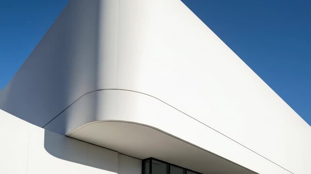 Architectural detail showcasing a modern building's white, curved facade meeting a bright blue sky, with deep shadows