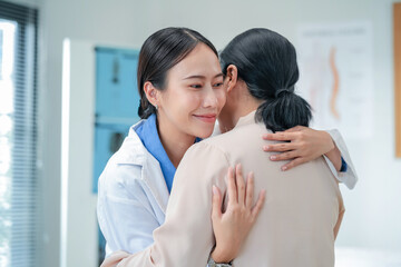 Happy Asian female doctor demonstrates compassionate care, holding hands with senior patient. Therapeutic touch approach showcases empathetic healthcare delivery and patient-centered emotional support