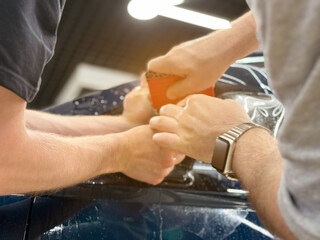 A car wrapping specialist applies a polyurethane film to the car. Detailer smoothes PPF. Car wrapping, detailing, tuning and styling. PPF protective film against chips and scratches. Car protection.