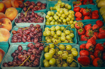 A vibrant assortment of fresh fruits is neatly arranged in small containers. The assortment includes ripe strawberries, juicy grapes, and peaches.