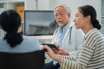 Asian daughter accompanies senior mother for medical consultation with doctor using digital health technology. Family centered care demonstrates intergenerational support and patient advocacy through