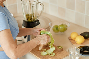 Woman peeling green apple with knife in kitchen, preparing fresh ingredients near blender, lemons,...