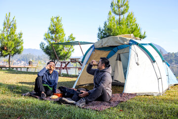 Two Men Relaxing and Drinking Coffee on a Blanket in Front of their Tent During a Camping Trip