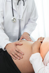 Doctor using hand for physical examination pregnant belly to check up baby and mother healthcare. Woman in 25 weeks of pregnancy visit gynecologist for regular examining health. Unrecognized people