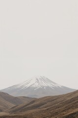 Fototapeta premium A serene and minimalist landscape view of a majestic snow-capped volcanic mountain against a pale, overcast sky
