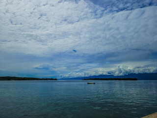 Beautiful seascape with small island, calm blue ocean, dramatic cloudy sky, and scenic tropical nature landscape for travel and nature photography.