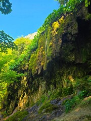 Moss ridden rocks at Sipote Waterfall in the forest with bright green branch trees and Bedeleu Mountain in the distance. Salciua, Alba, Romania