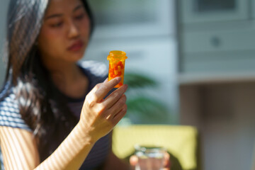 Woman holding a prescription bottle and glass of water, contemplating the decision to take her...
