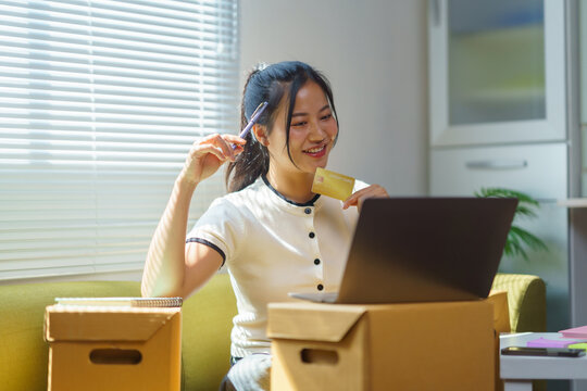 Happy entrepreneur enjoying online shopping with a credit card and laptop in a stylish new home office filled with natural light