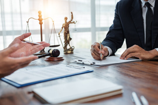 Lawyer and client discussing terms and conditions while signing legal document in office with gavel and justice scales in background