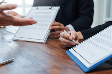 Business partners signing a contract at an office desk, finalizing a deal and solidifying their...