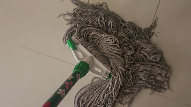 well-used, tangled string mop head resting on a light-colored, tiled floor, suggesting a pause during household cleaning or maintenance.