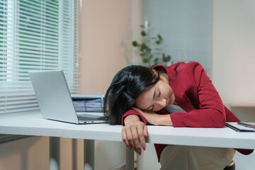 Young Asian manager resting on table after hard working day, suffering from chronic fatigue or...
