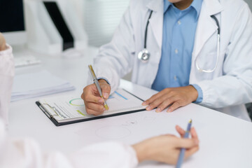 Doctor pointing at medical chart while explaining diagnosis and treatment plan to patient during...