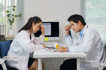 Two worried doctors experiencing headaches and taking notes while managing their demanding tasks in...