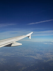 View from an airplane window over the wing, capturing a clear blue sky, a thin contrail, and the vast, blurred patchwork of land below, symbolizing air travel, freedom, and distant destinations.