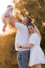 Fototapeta premium Happy family enjoys golden hour outdoors with their baby daughter