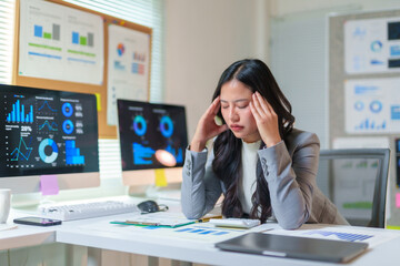 Young professional woman suffering from headache while analyzing financial charts and graphs on...